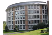 Curved multi-story residential building with rows of windows overlooking a grassy lawn and benches.