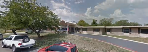 Exterior view of Arbor Grace Guest Care Center with driveway, parking, and trees.