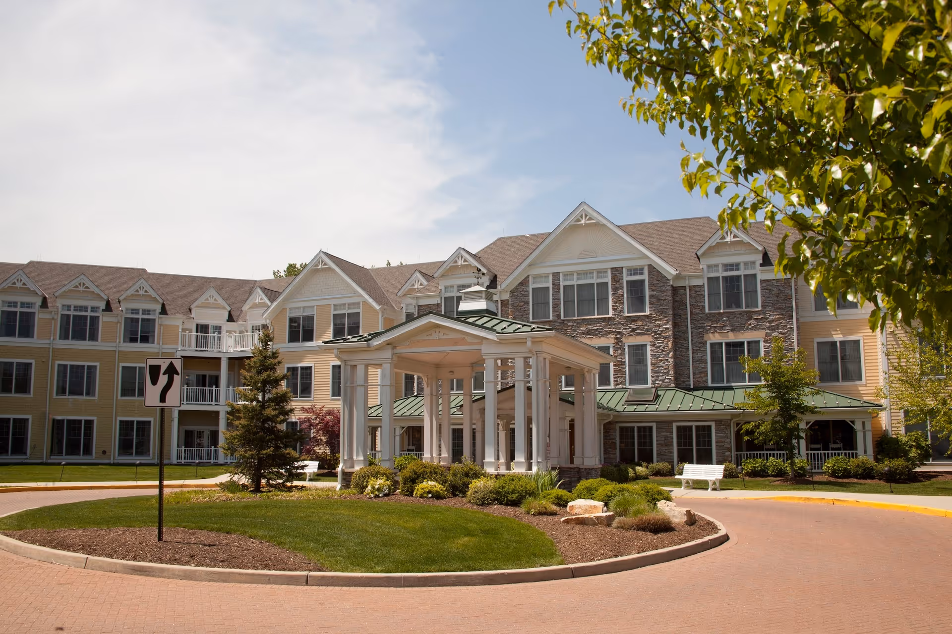 Front exterior of a multi-story senior living building with a covered entrance portico, circular driveway, and landscaped grounds.