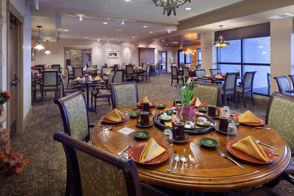 Spacious communal dining room with multiple set tables and chairs, featuring a round table in the foreground set for a meal.
