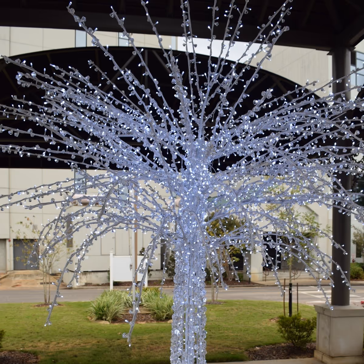 Decorative illuminated white LED tree sculpture displayed under a covered entrance in front of a building.