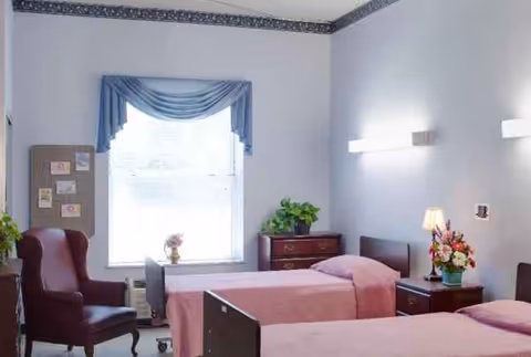 Two pink-covered beds with nightstands and a window in a pastel senior living bedroom.