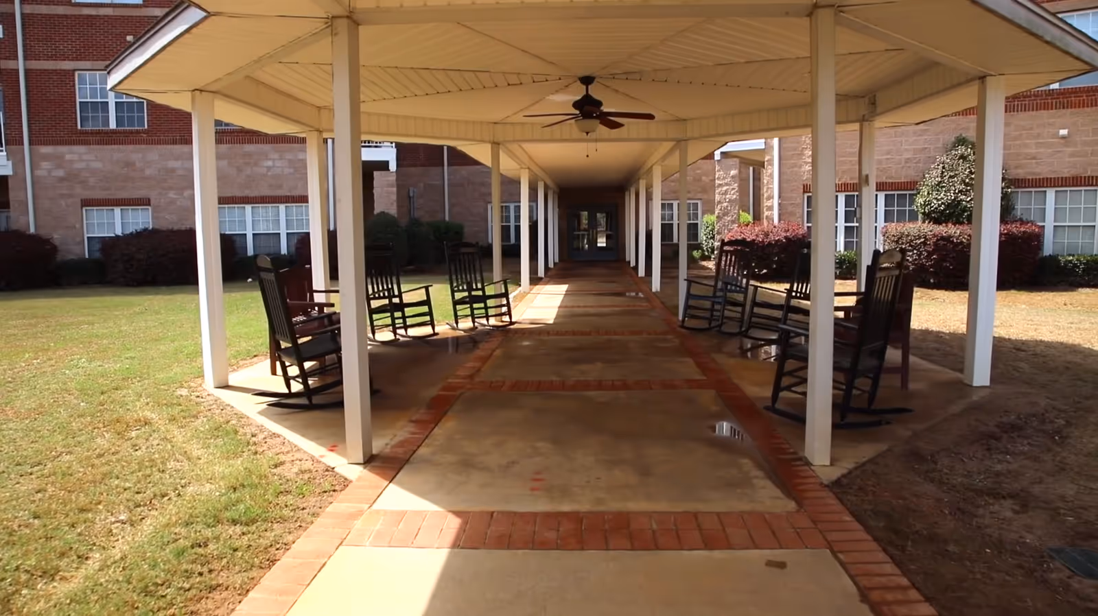 Covered outdoor walkway lined with rocking chairs leading to the building entrance.