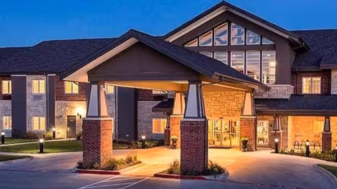 Two-story building with an illuminated covered entrance (porte-cochere) and large windows at dusk.