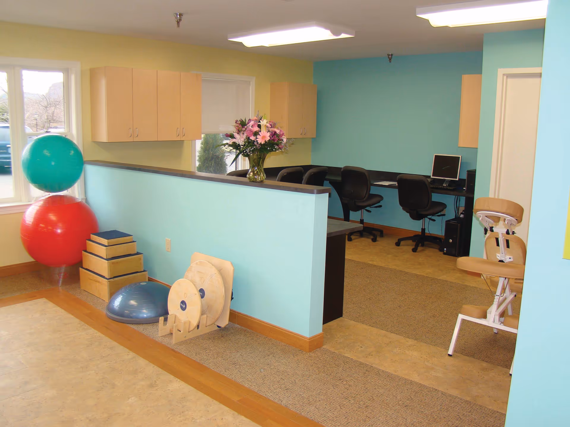 Interior therapy/reception area with exercise equipment, a low turquoise partition, and computer workstations.