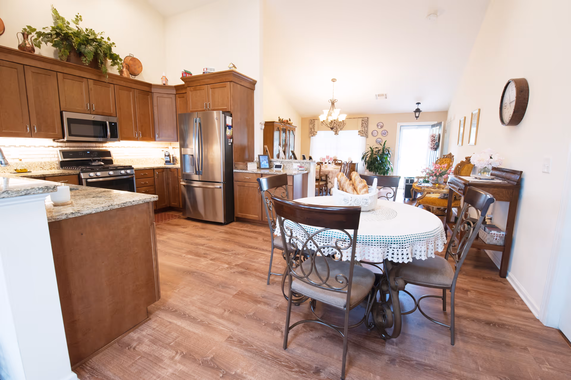 Open-plan kitchen and dining area with wooden cabinets, stainless-steel appliances, and a round table with chairs.