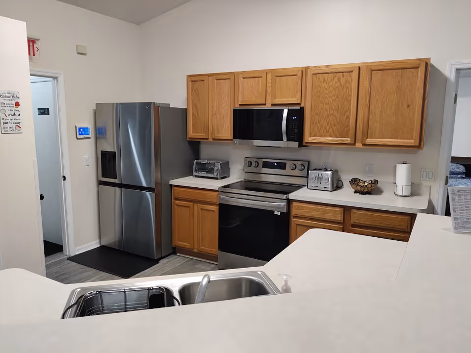 Clean kitchen with stainless steel refrigerator, stove and microwave, oak cabinets, countertop appliances, and a sink in the foreground.