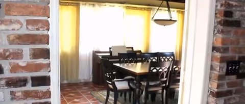 Indoor dining area with a wooden table and six chairs, brick walls and hanging light.