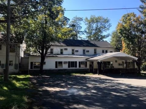 Front view of Narrowsburg Homes, a two-story white senior living building with a carport.