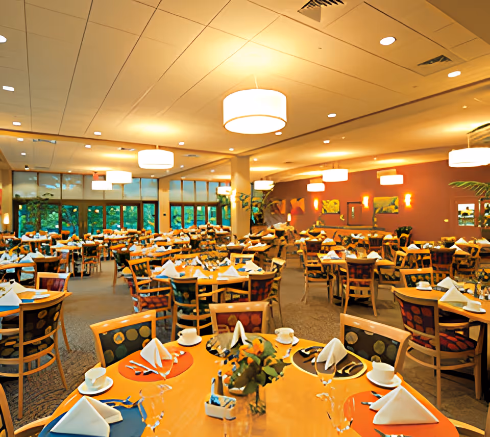Spacious, well-lit dining room with many tables and chairs set with plates, cups, and folded napkins.