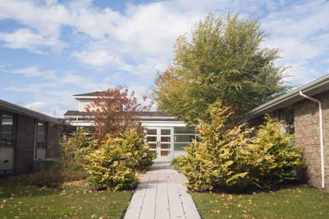 Pathway lined with shrubs leads to glass doors at a senior living facility.