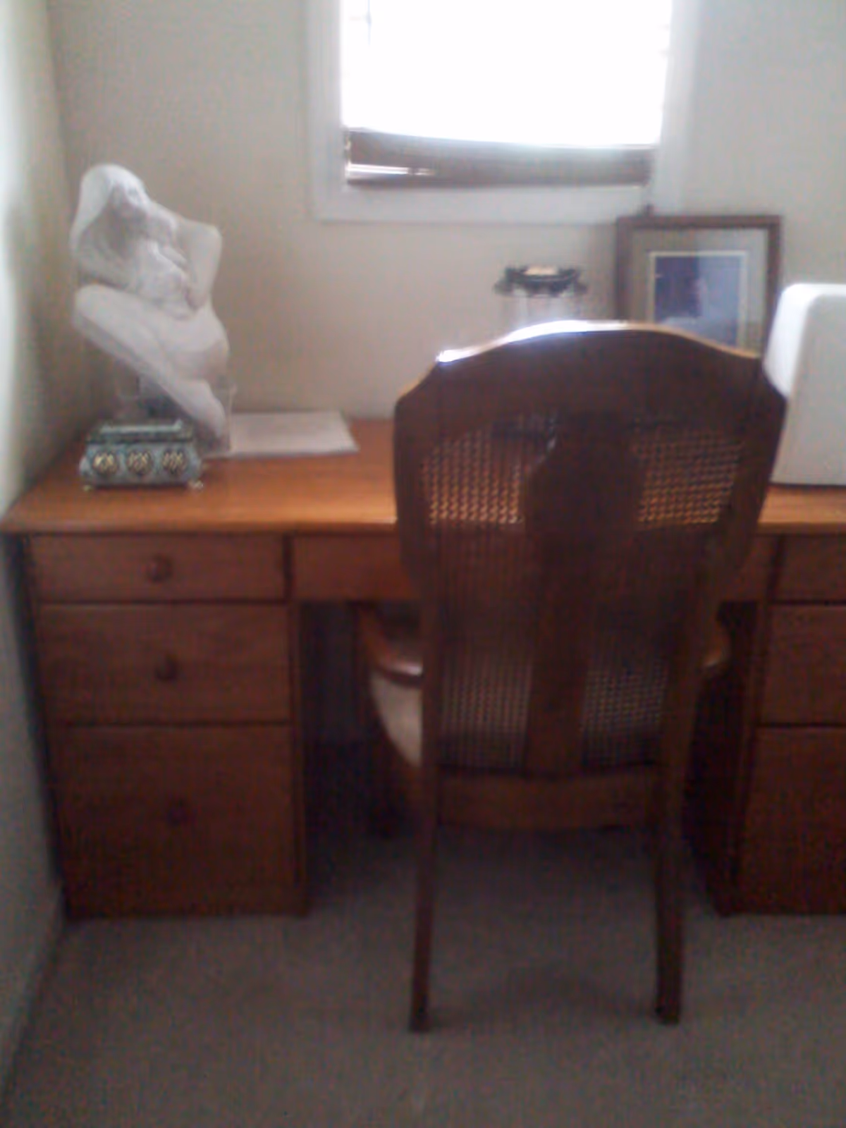 Wooden desk with drawers and a carved chair beneath a small window, with decorative items on the desk.