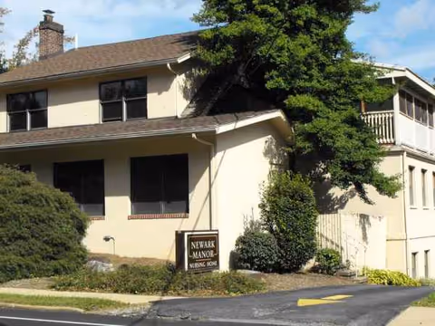 Beige two-story nursing home exterior with Newark Manor sign and greenery.