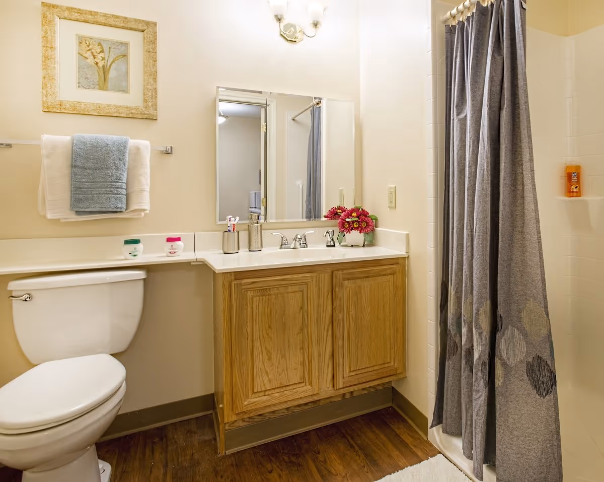 Clean, well-lit bathroom with a toilet, wooden vanity and sink with mirror, towel rack, and a shower with a gray curtain.