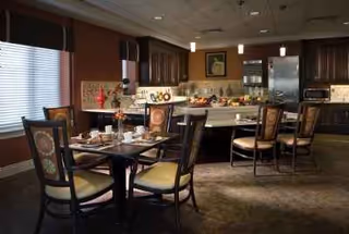 Senior living dining room with tables set for meals and a kitchen buffet in background.