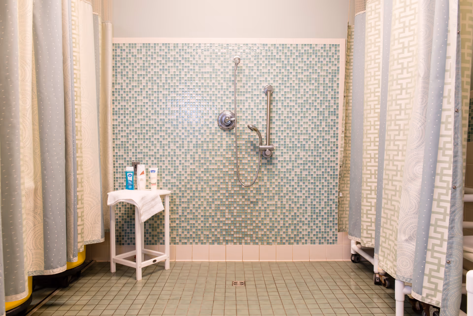 A shower area with a mosaic wall and shower fixtures, enclosed by patterned curtains.