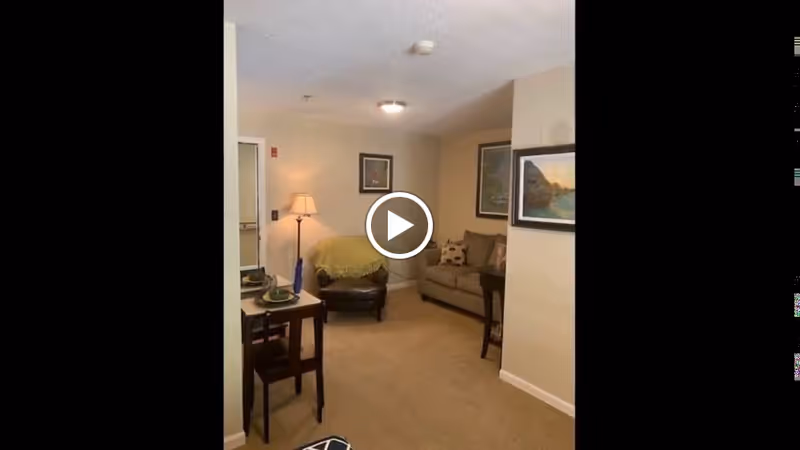 Cozy living area with a sofa, armchair, floor lamp, small dining table and framed artwork on the walls.