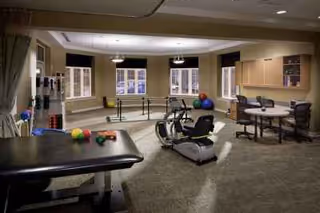 Rehabilitation gym with exercise equipment, therapy chairs, and a desk in a spacious interior.