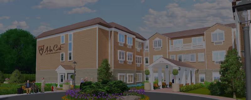 Exterior view of Amber Court Assisted Living in Elizabeth, showing a three-story building with beige siding and stone accents. The entrance features a covered porch with white columns and benches. There are landscaped gardens with green bushes and purple flowers, and a few people are visible near the entrance and along the walkway.