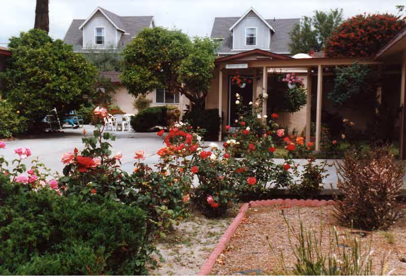 Exterior view of Hanover Guest Home with a garden of blooming roses, a paved path, and a covered entrance.