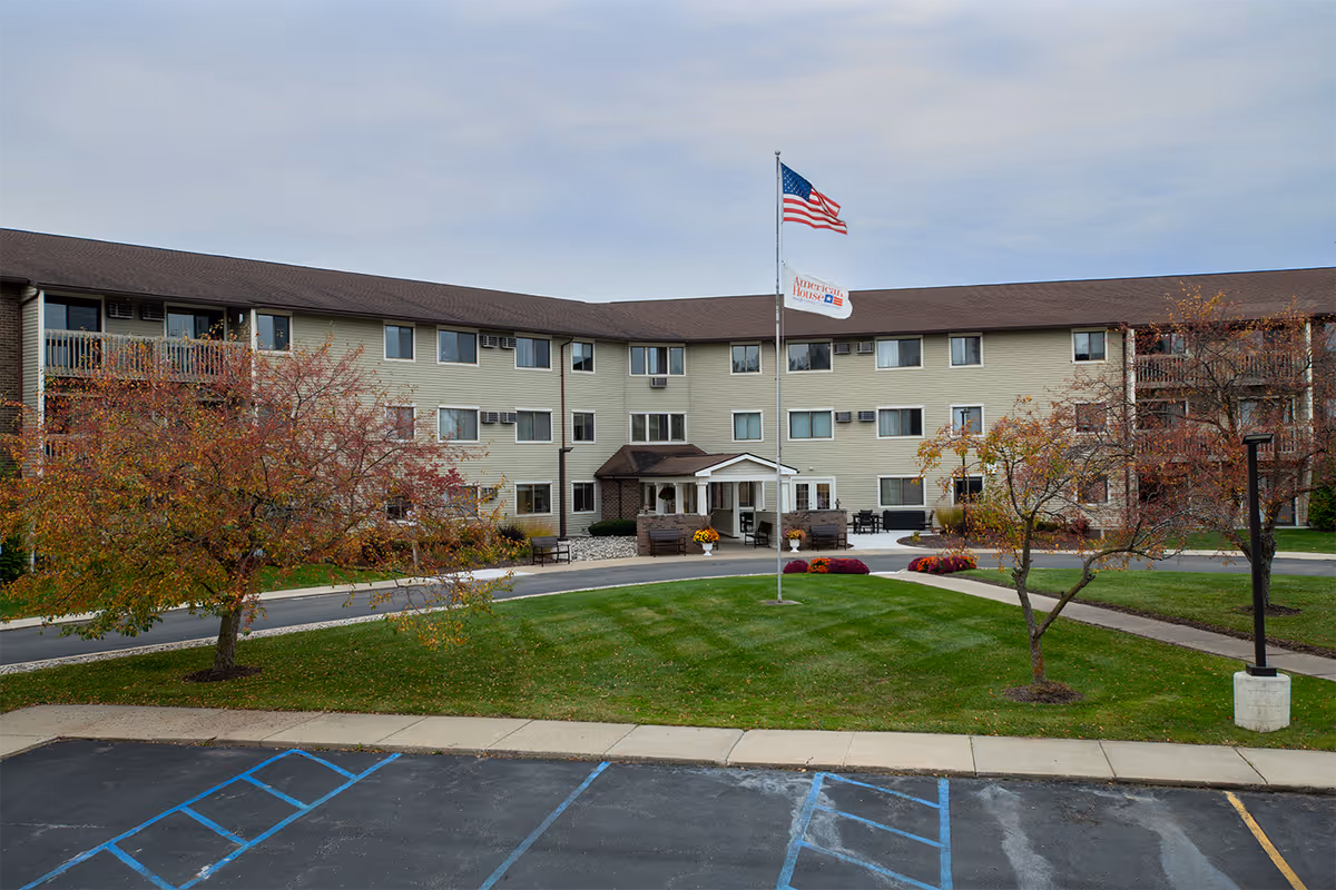 Front exterior of a three-story senior living building with an American flag and landscaped lawn.