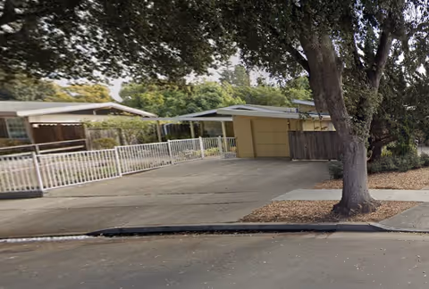 Exterior view of a single-story senior care facility with a gated drive and trees.