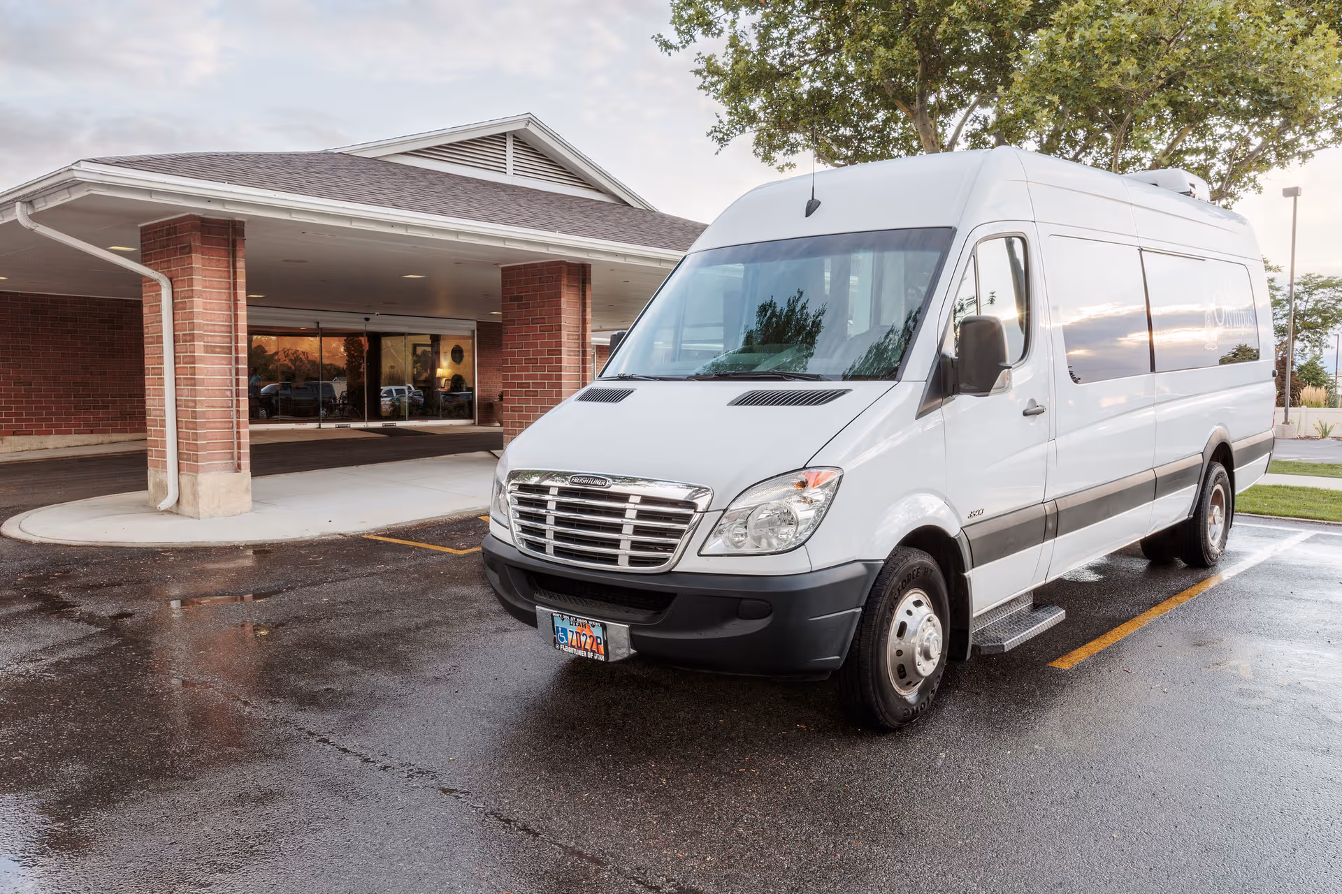 A white passenger van parked in front of the entrance to a brick building with a covered drop-off area, likely at a rehabilitation center.