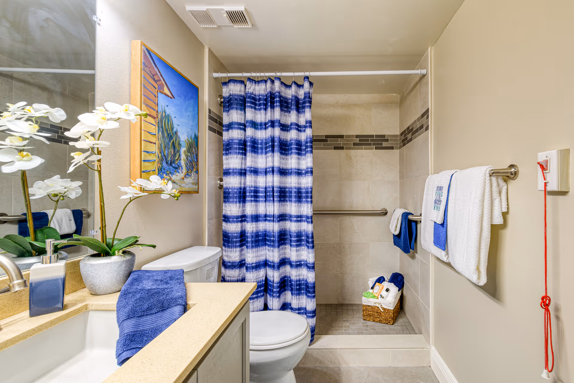 Bathroom featuring a sink and vanity, toilet, walk-in tiled shower with a blue-striped curtain, and blue towels.