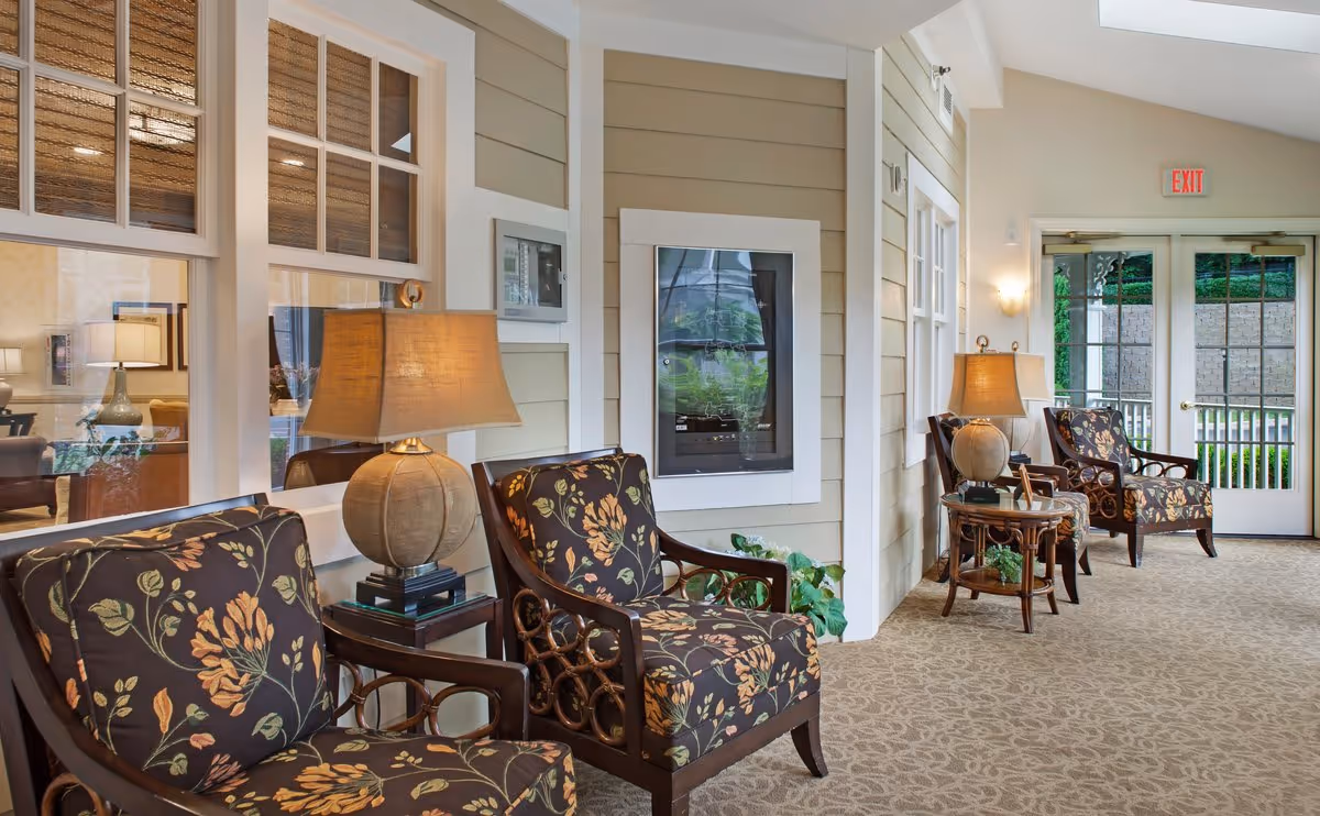 Carpeted lounge corridor with floral-upholstered chairs, side tables and lamps beside glass doors.
