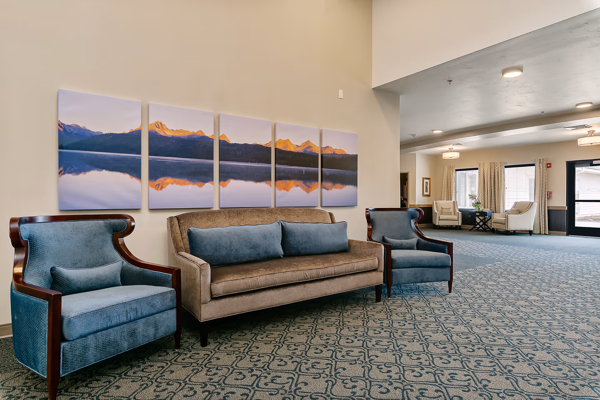 Spacious senior living lobby with a sofa and two blue armchairs under multi-panel mountain artwork.