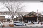 Exterior view of Westhills Village facility entrance during winter with snow on the ground and a few parked cars in front. A leafless tree is visible near the entrance, and an American flag is flying on a flagpole to the right.