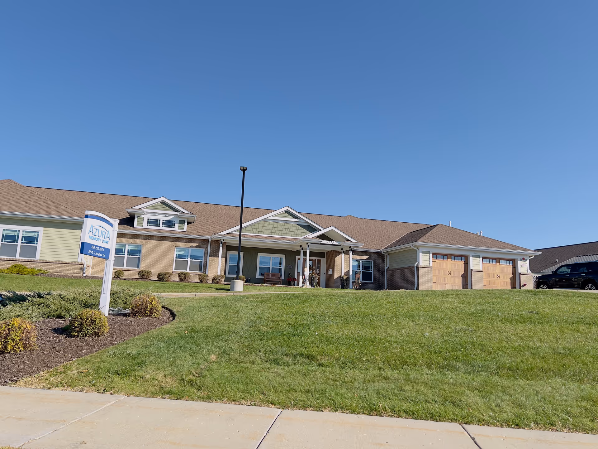 Front exterior of a single-story memory care building with a lawn, entrance canopy, and an 'Azura' sign under a clear blue sky.
