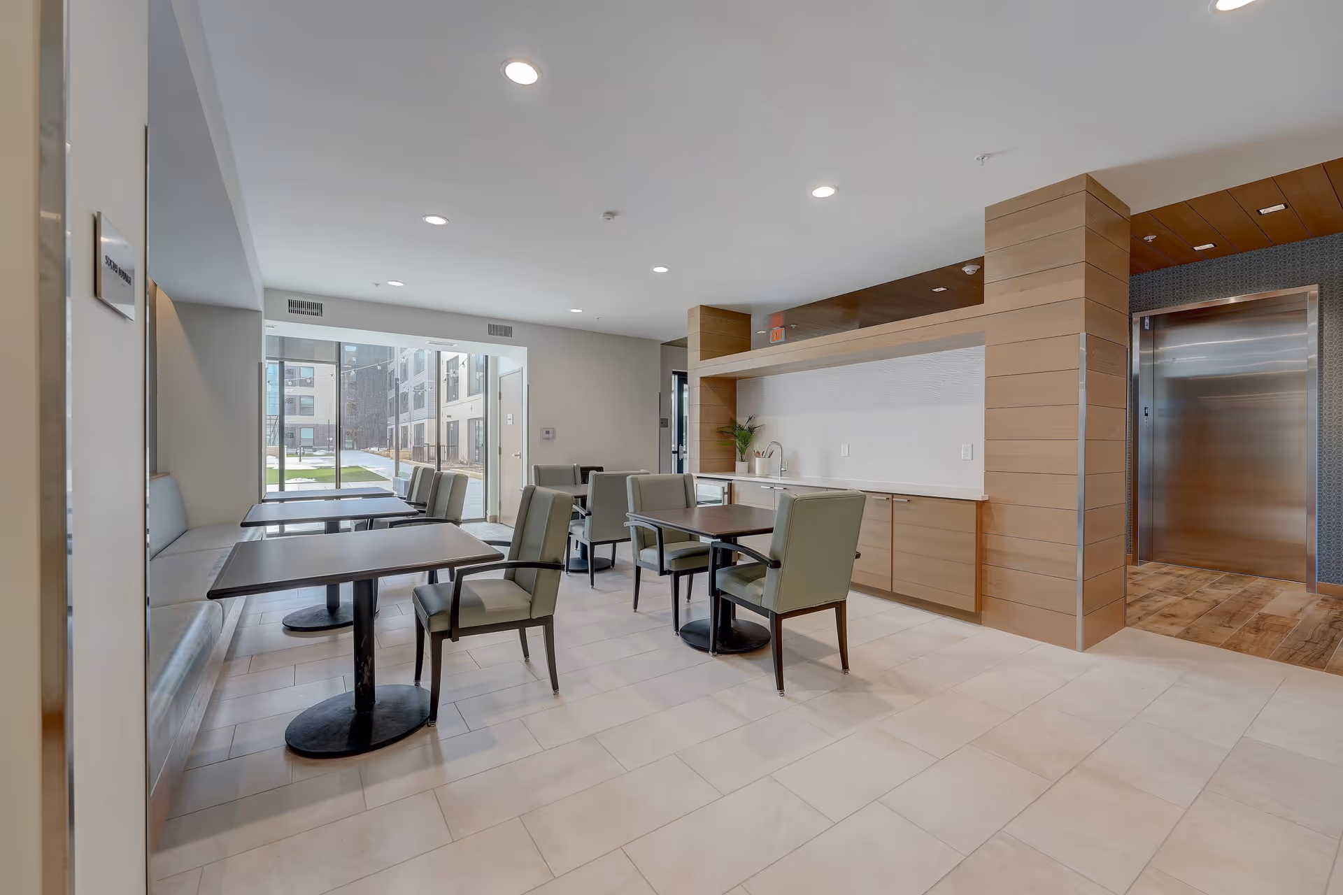 Bright communal dining area with multiple tables and chairs, a serving counter, and an elevator.