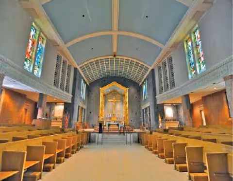Interior of a chapel with pews, altar, cross, and stained-glass windows.