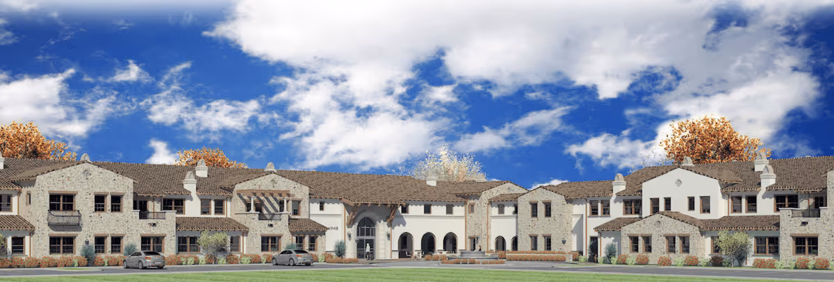 Front exterior view of Villa Lorena Senior Living facility showing a large two-story building with stone and stucco facade, multiple windows, balconies, and a central entrance under a blue sky with scattered clouds.