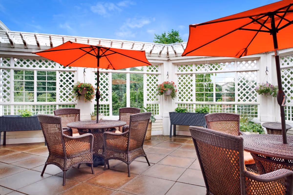 Outdoor patio with wicker tables and chairs under orange umbrellas next to white lattice walls and hanging plants.