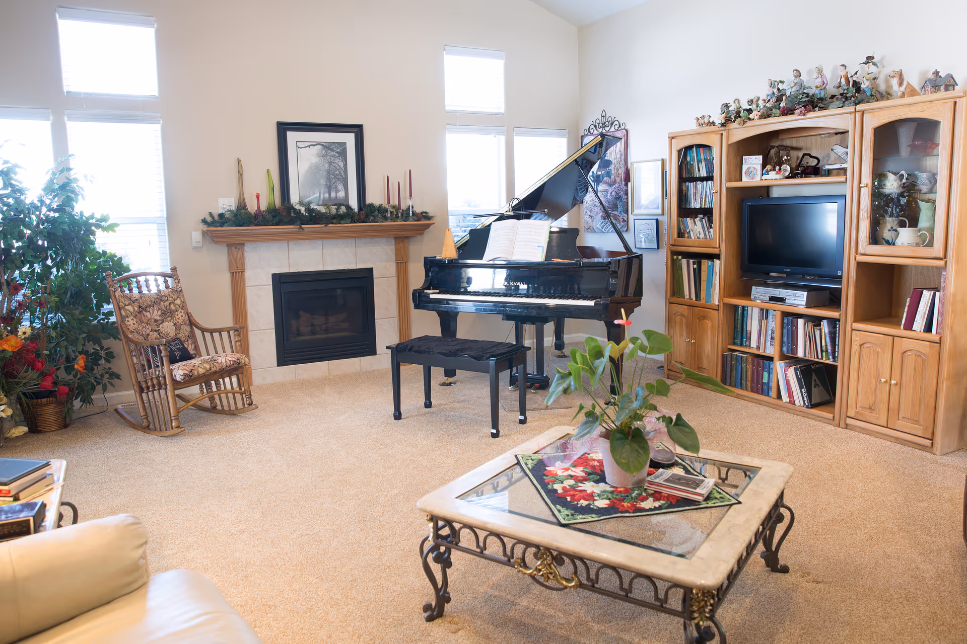 Bright living room featuring a grand piano near a fireplace, rocking chair, coffee table, and wooden entertainment center.