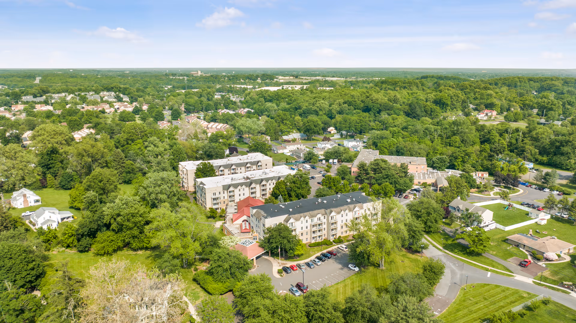 Aerial view of the Oxford Enhanced Senior Living campus showing multi-story residential buildings, a parking lot, and surrounding trees and neighborhood.
