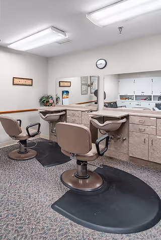 Interior salon area with two styling chairs and wash basins in front of a large mirror and cabinetry.