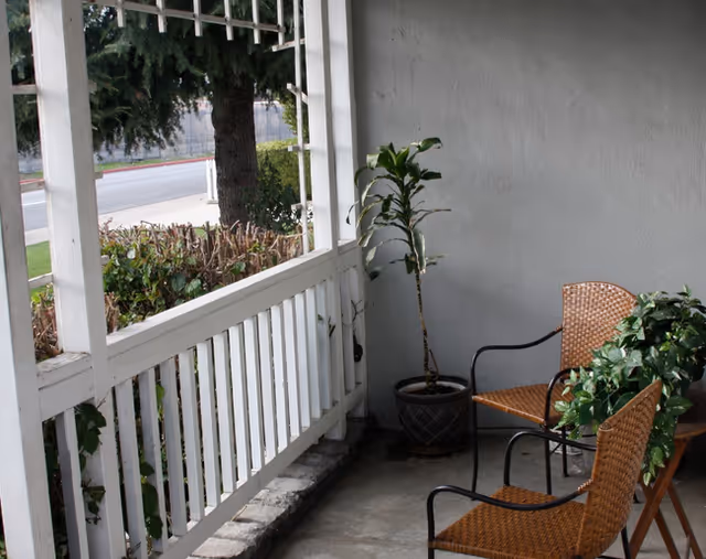 Outdoor porch with wicker chairs, potted plants, and white railings.