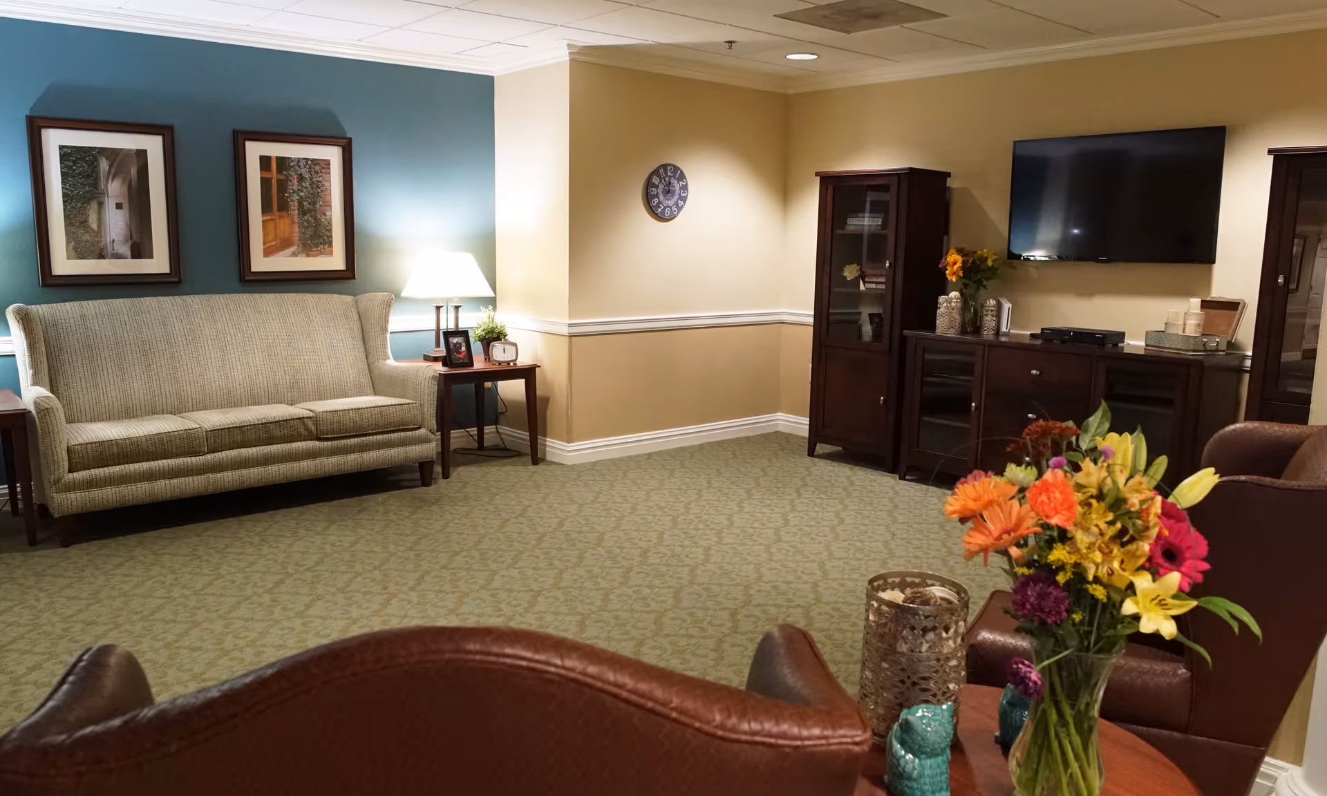 Comfortable sitting room with a sofa, armchairs, a TV and cabinets, and a vase of flowers on a table.
