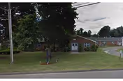 Single-story brick senior living building with a front lawn, trees, and a curved driveway entrance.