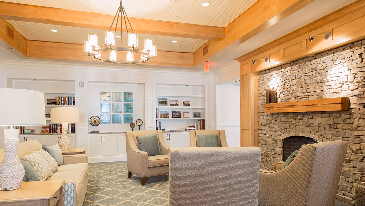 Cozy living room with upholstered chairs and sofa, a chandelier, built-in bookshelves, and a stone fireplace.