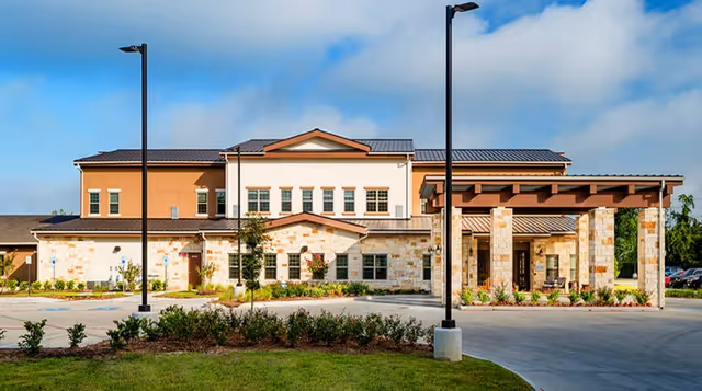 Front exterior of a two-story stone and stucco senior living facility with a covered entrance and driveway.