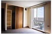 Empty bedroom with carpet, a built-in closet with sliding wooden doors, and a large window overlooking the neighborhood.