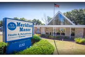 Front exterior of Meridian Manor Health & Rehabilitation Center showing the entrance canopy and a blue sign with the facility name and address.