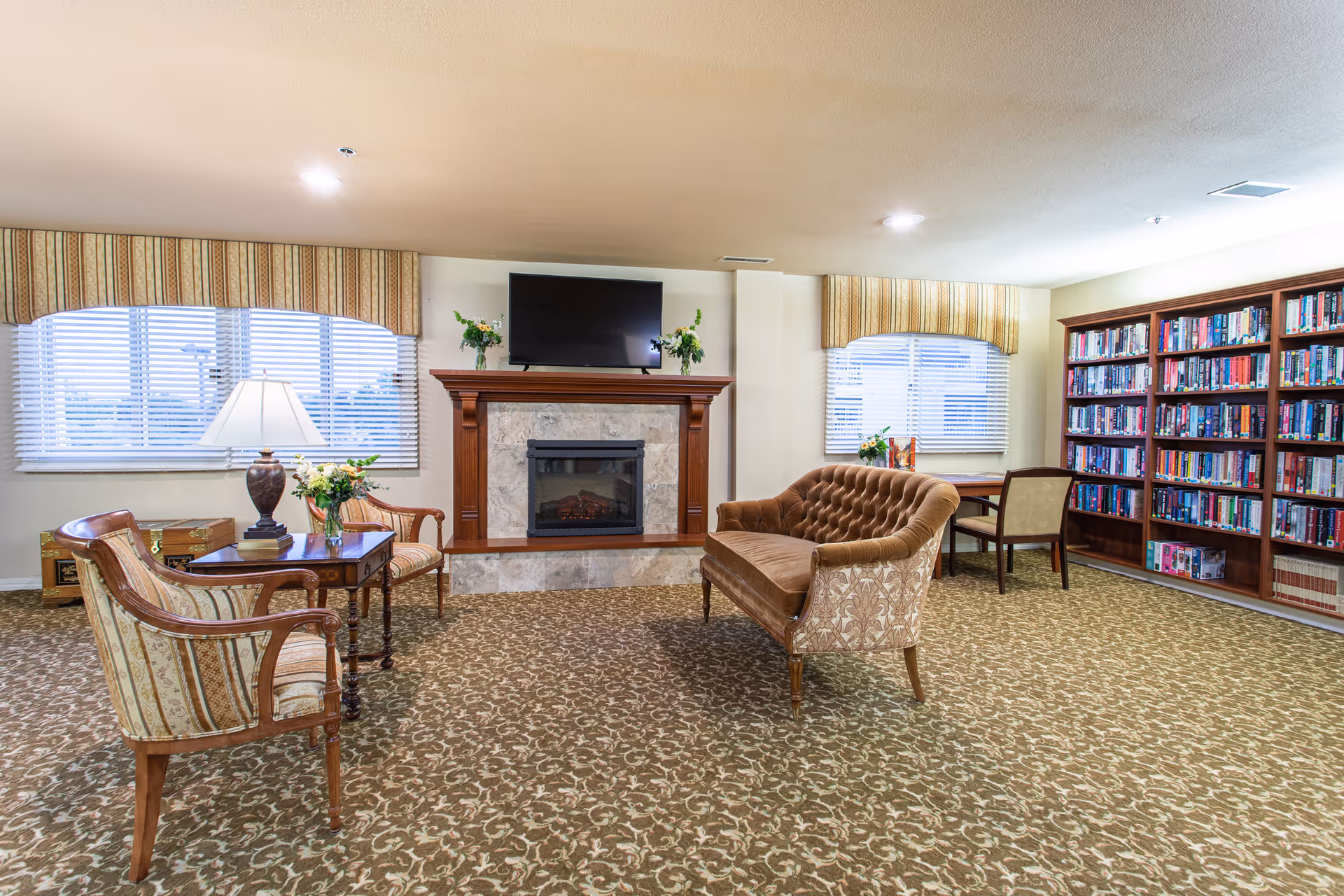 Comfortable lounge with a fireplace and TV, upholstered seating, a coffee table, and bookshelves.