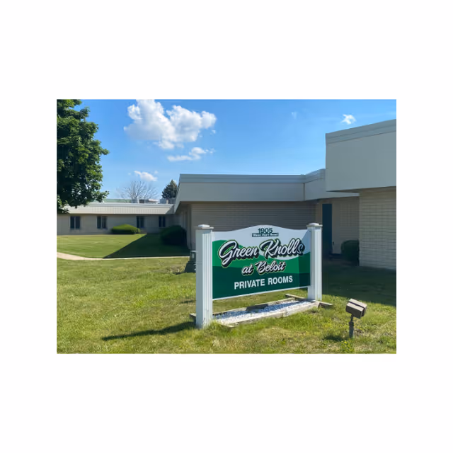 A lawn sign reading "Green Knolls at Beloit - Private Rooms" in front of a single-story building under a blue sky.