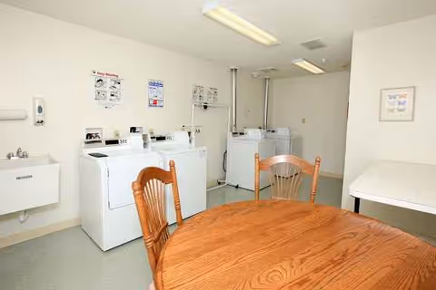 Communal laundry room with washing machines along the wall and a round wooden table with chairs.