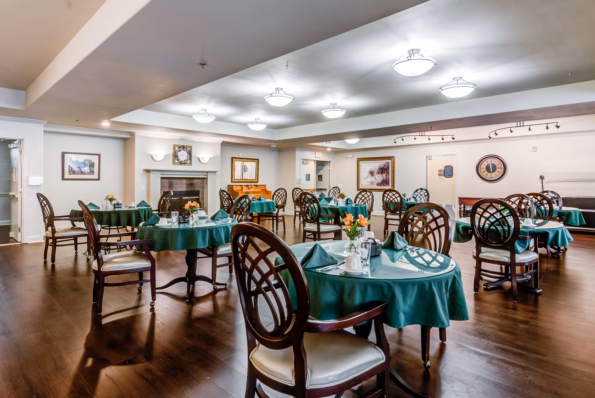Dining room with round tables covered in green tablecloths and wooden chairs set for meals.